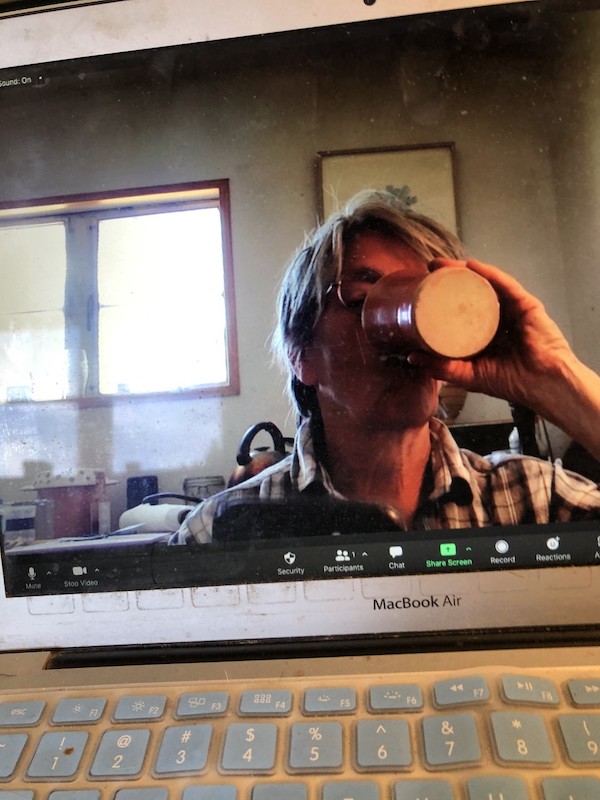 Eileen drinking from a cup that obscures their face, seen from a photo they took of them on Zoom on their laptop screen